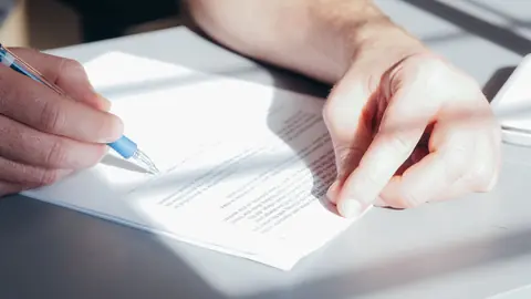 A hand signing a document with a blue pen